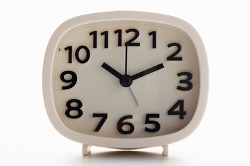 Small white alarm clock, black numbers, set the time for 10.10 o'clock, placed on a white table.