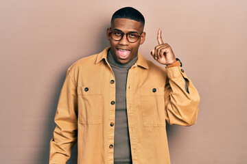 Young black man wearing casual clothes and glasses pointing finger up with successful idea. exited and happy. number one.