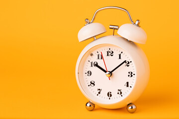 Small white alarm clock, black numbers, set the time placed on a table. Clock on isolated yellow background.