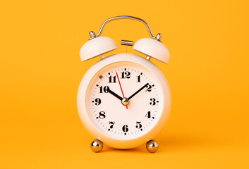 Small white alarm clock, black numbers, set the time placed on a table. Clock on isolated yellow background.