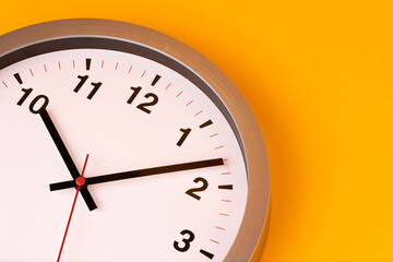 Large white alarm clock, black numbers, set the time placed on a table. Clock on isolated yellow background.