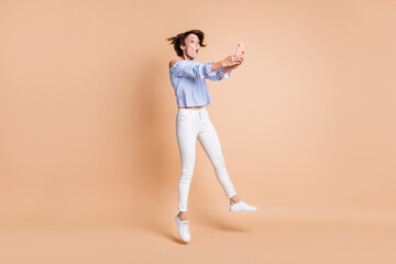 Fototapeta na wymiar Full size photo of young excited surprised girl jump up make take self photo selfie isolated over beige color background
