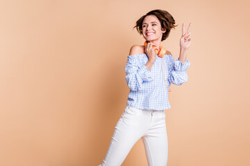 Obraz premium Photo of young excited girl happy smile show peace cool v-sign hold headphones look empty space isolated over beige color background