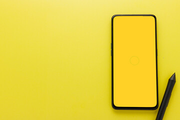 Flat lay. Top view black smartphone with blank yellow screen and pen mouse on yellow background with copy space, workspace.