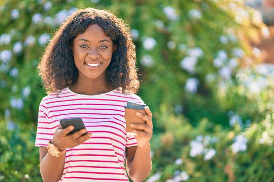 Young african american girl using smartphone drinking coffee at the park.