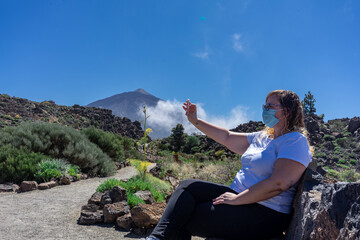 Naklejka premium Young tourist woman with mask taking a selfie. In the background you can see Mount Teide, with its 3,178 meters high. This volcano is located in Tenerife, Canary Islands
