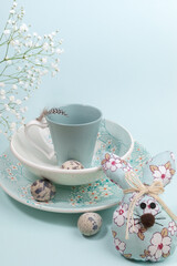 Easter festive composition for breakfast with beautiful tableware, quail eggs, DIY textile Easter bunny on light blue.