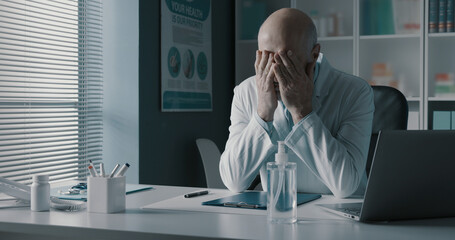 Stressed exhausted doctor with head in hands