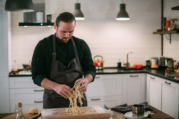 A male chef prepares noodles at home in the kitchen.