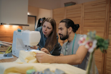 Obraz na płótnie Canvas A man sews on a sewing machine, a woman explains how to sew. Family home hobby.