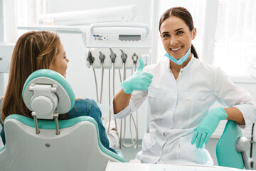 European mid dentist woman showing thumb up while working with patient - obrazy, fototapety, plakaty