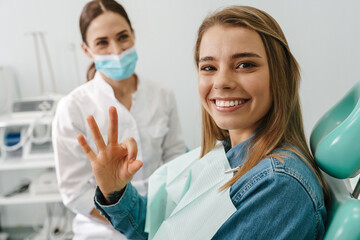 European young woman showing ok sign while sitting in medical chair