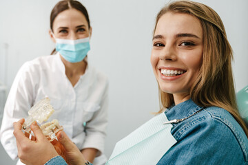 European mid happy dentist woman showing teeth imitation to her patient