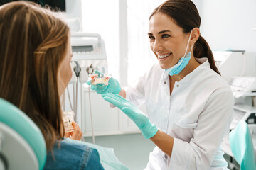 European mid happy dentist woman showing teeth imitation to her patient
