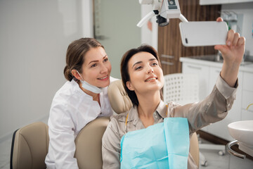 Young beautiful medical doctor, dentist, hygienist or orthodontist and her patient taking selfie...