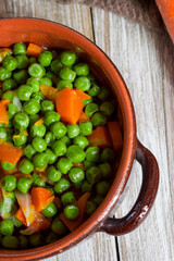 Green peas and carrots in small pan on wooden background.