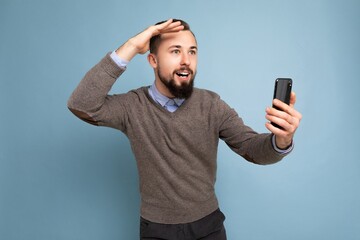 closeup of Handsome smiling brunette bearded man wearing grey sweater and blue shirt isolated on background wall holding credit card looking to the side