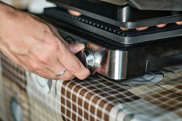 Man's hand lays out raw sausages on the grill
