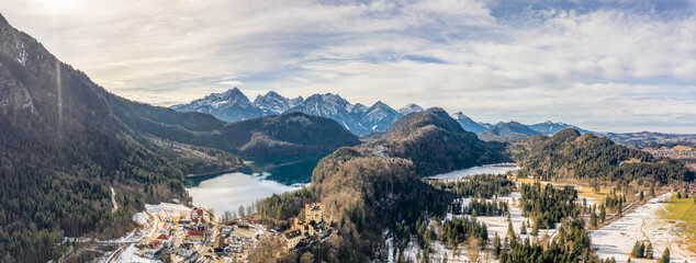 Aerial panorama drone shot of Hohenschwangau by lake in Fussen with view of Alps snow mountain range in Germany winter