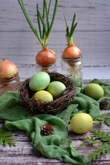 Painted Easter eggs on a green napkin and young green onions in glass jars on a wooden background.