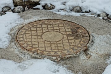 one rusty iron manhole on gray concrete in a snowdrift of white snow 