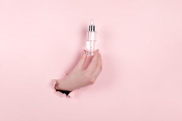 Glass Bottle in female hand with fluid collagen and hyaluronic acid, hydration skin. Copyspace Abstract pink background.