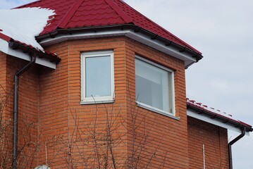 attic of a brown private house with windows under a red tiled roof with white snow outside