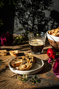 Homemade almond and chocolate biscotti with glass of coffee and  ranunculus flowers on wooden table on dark background.