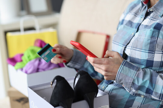Woman is sitting on couch with box of shoes and holding bank card and smartphone