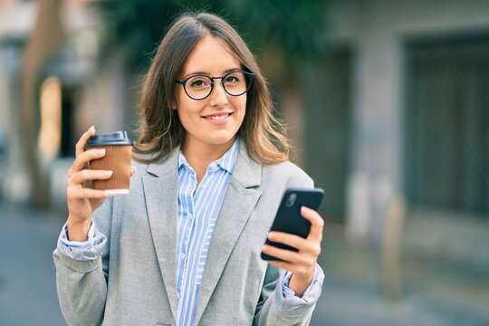 Young hispanic businesswoman using smartphone and drinking take away coffee at the city.