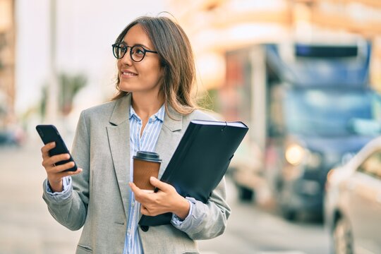 Young hispanic businesswoman using smartphone and drinking take away coffee at the city.