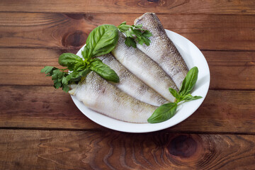 Uncooked notothenia fish, greens on dish on rustic table