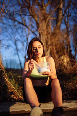Young sporty woman eating healthy lunch in the field at the sunset