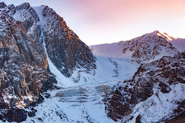 Scenic aerial view over Aktru glacier, high in the mountains, covered by snow and ice during beautiful pink color sunset. Altai winter landscape, Russia