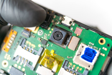 Fix the phone.A technician or master repairs a mobile phone, he installs and changes the camera in the motherboard. Hands, gloves, macro