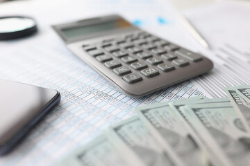 American banknotes, along with financial statement and calculator, lie on table