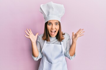 Young beautiful woman wearing professional cook uniform and hat celebrating crazy and amazed for...