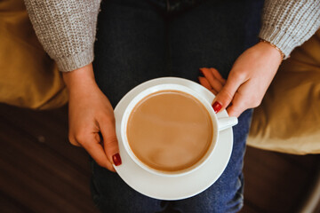 A white cup of coffee in the girl's hands. Cozy and atmospheric photo. Winter warm drink.