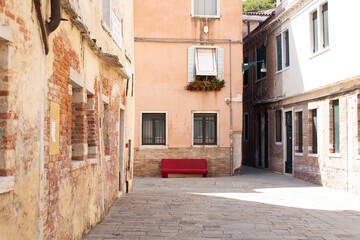 Red abandoned couch in a Venetian street with old buildings in a sunny day