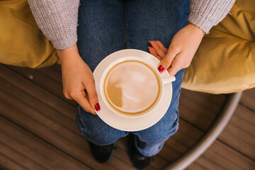 Fototapeta na wymiar A white cup of coffee in the girl's hands. Cozy and atmospheric photo. Winter warm drink.