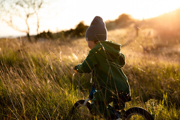 A little boy is riding a balance bike in the park at sunset.