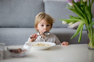 Cute toddler boy, eating pasta with white cheese at home