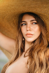 Gorgeous young woman in a big straw hat with long blond hair in a lavender field at sunset