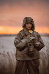 A young woman with a flower in her hands. The woman in the protective suit took off her gas mask. On the background of a sandy area. The concept of radioactive contamination and environmental disaster