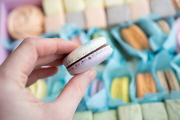 Sweet tooth. Hand holding macaron over a box of sweets. Hand holding macaroon over a confectionery gift box