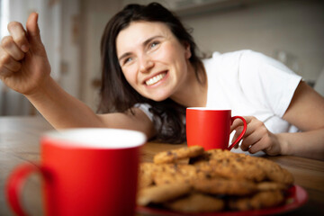 Young woman drinks coffee with cookies at home kitchen.