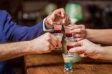 Cocktail at the nightclub. Group friends tequila shot glasses in bar. Male hands glasses of shot or liqueur. Friends drink shot or liqueur. Five glasses of alcohol.Tequila shots, vodka, whisky, rum