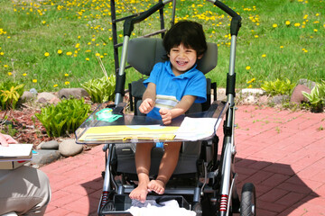 Disabled two year old boy having therapy in wheelchair outdoors