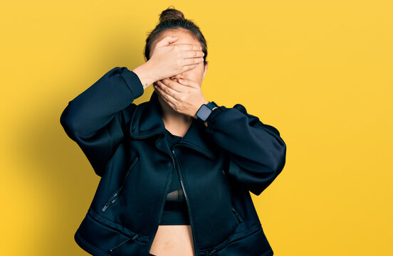Young hispanic girl wearing sportswear covering eyes and mouth with hands, surprised and shocked. hiding emotion