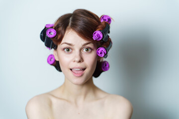 young woman with purple curlers on her head naked shoulders gray background